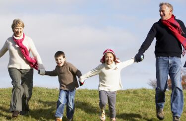 Großeltern rennen beschwerdefrei mit ihren Enkeln einen grünen Hügel hinunter