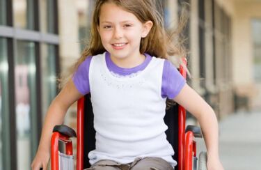 ein kleines Mädchen sitzt in einem roten Rollstuhl und lächelt - mit angepassten Rollstühlen von o.t.n wird das Leben leichter